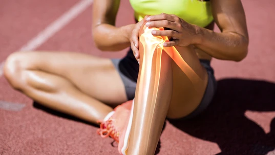 Low section of female athlete suffering from knee pain while sitting on track during sunny day